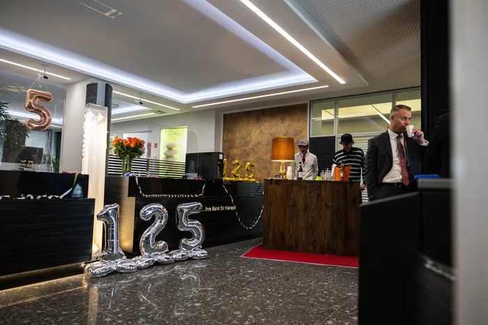 Festlich dekorierter Schalterraum der Volksbank Kierspe mit silbernen Zahlen „125“ und einem Mann mit Anzug, der ein Getränk hält.
