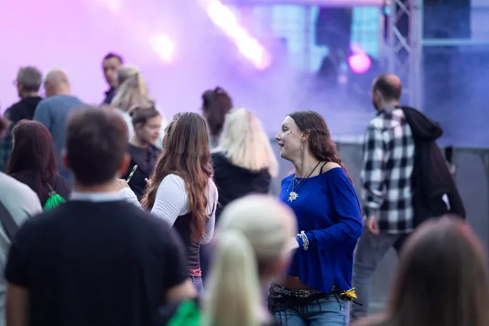 Eine junge Frau in einem blauen Oberteil steht in einer Menschenmenge vor einer lila beleuchteten Bühne beim Bautz 2026 Festival.