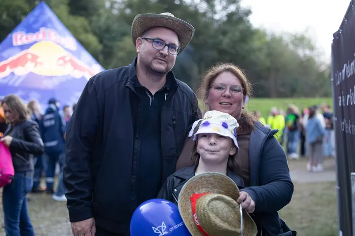 Ein Mann mit Strohhut, eine Frau und ein Kind lächeln vor einem blauen Red Bull Zelt.