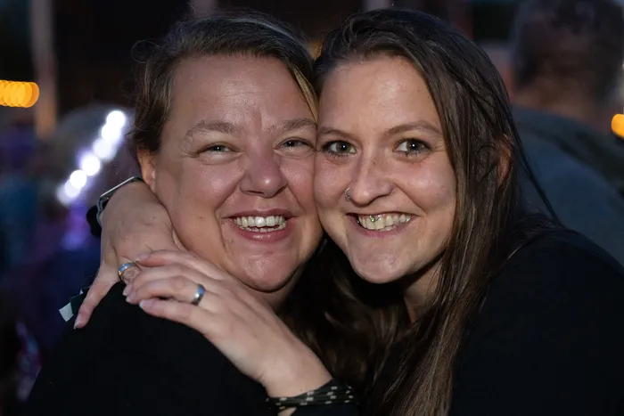 Zwei lächelnde Frauen umarmen sich eng bei einer Veranstaltung im Freien bei Nacht.