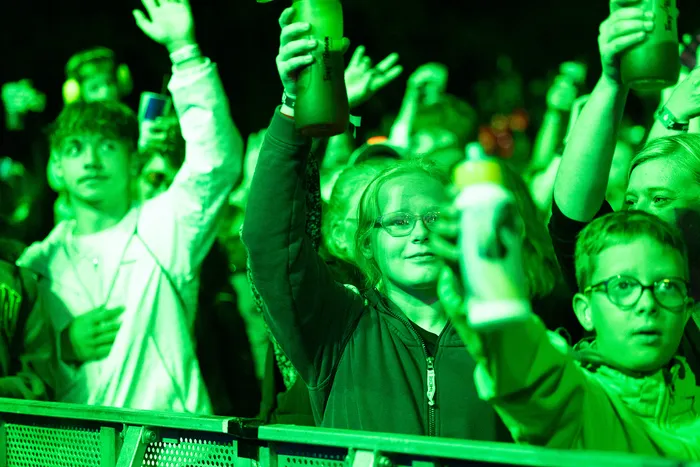 Eine Menschenmenge unter grünem Licht mit erhobenen Händen und Flaschen bei der Turntable Stage.
