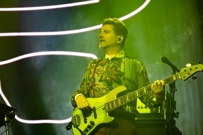 Jan Delay spielt auf einer Bühne mit grünem Licht und hellen Lichtbögen im Hintergrund Bass.