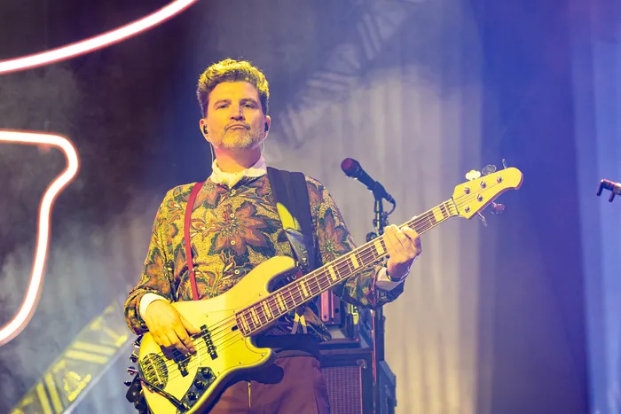 Jan Delay spielt auf der Bühne eine E-Bass-Gitarre. Er trägt ein gemustertes Hemd und rote Hosenträger.