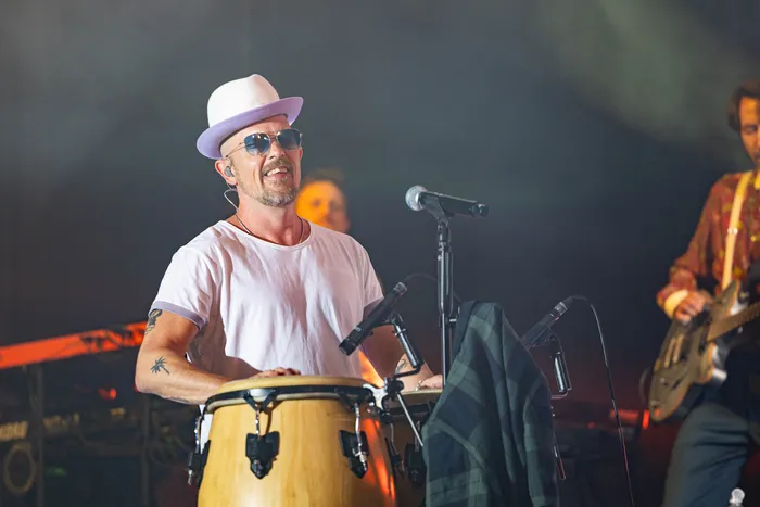 Jan Delay mit weißem Hut und Sonnenbrille spielt Congas auf einer Bühne bei einem Live-Auftritt.