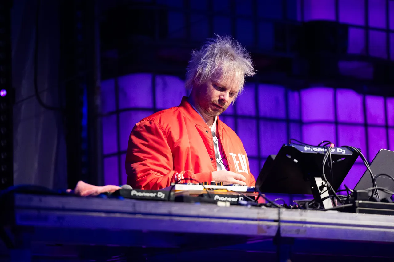 Jan-Christian Zeller in einer roten Jacke bedient an einem DJ-Pult die Turntables unter violettem Bühnenlicht.