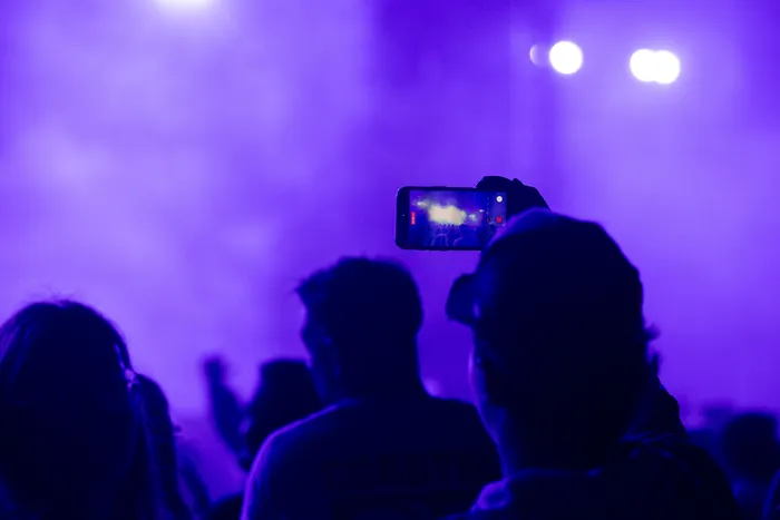 Silhouette einer Person, die mit einem Smartphone eine Bühne unter violettem Licht filmt.