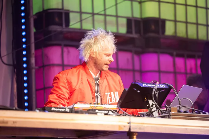 Jan-Christian Zeller mit stacheligen blonden Haaren und einer roten Jacke bedient DJ-Equipment an der Turntable Stage.