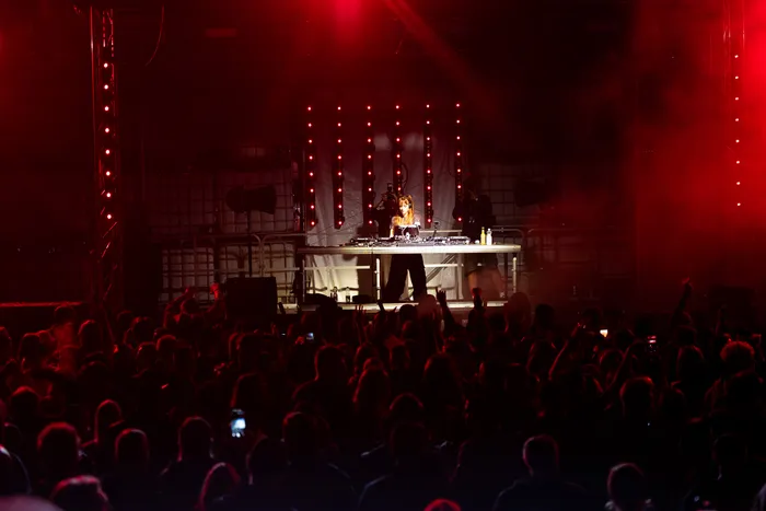 Ein DJ performt an einem Turntable auf einer Bühne unter intensivem rotem Licht vor einer großen Menschenmenge.