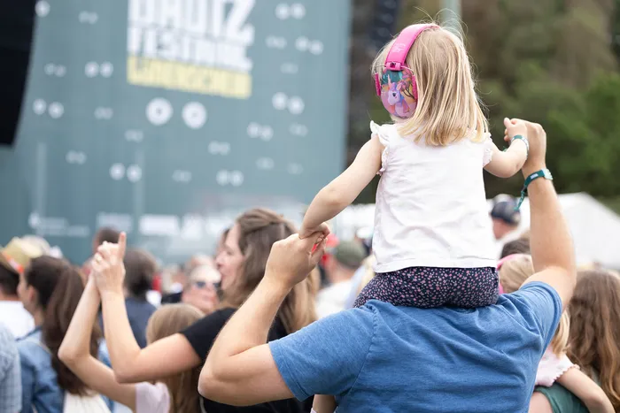 Ein Kind mit rosa Kopfhörern sitzt auf den Schultern eines Mannes und blickt auf die Bühne des Bautz Festivals.