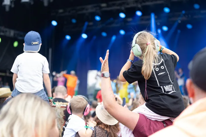 Ein Kind mit hellgrünen Kopfhörern sitzt auf den Schultern einer Person vor einer Bühne mit blauen Scheinwerfern beim Bautz 2026 Festival.