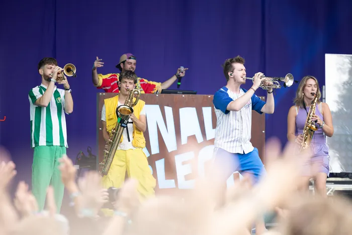 Die Brassband Knallblech spielt mit Trompeten und Saxophonen auf einer Bühne vor einem blauen Hintergrund.