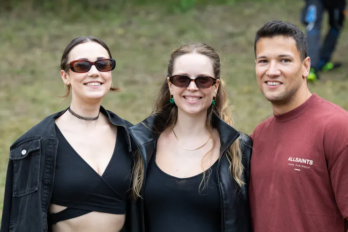 Zwei Frauen mit Sonnenbrillen und ein Mann im weinroten T-Shirt lächeln in die Kamera.