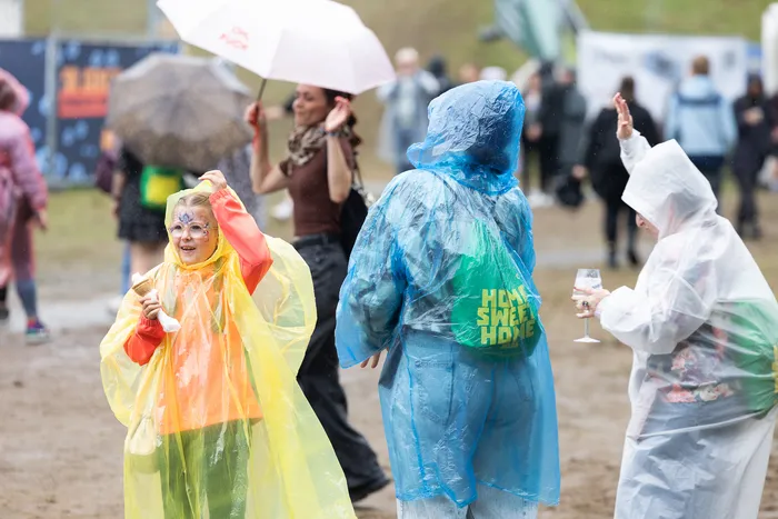 Ein Kind in einem gelben Regenmantel und andere Besucher in Regenbekleidung auf einem Festivalgelände bei regnerischem Wetter.