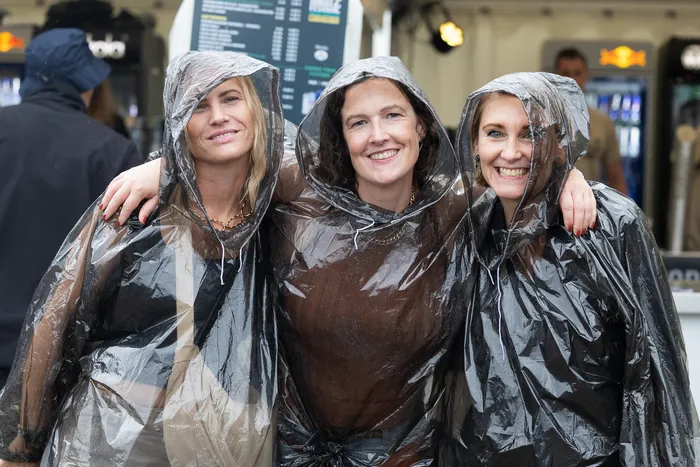 Drei lächelnde Frauen tragen transparente Regenponchos mit Kapuzen.
