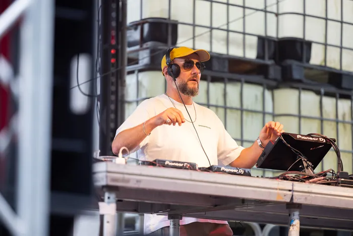 Ante Perry mit gelber Kappe, Sonnenbrille und Kopfhörern bedient ein DJ-Pult.