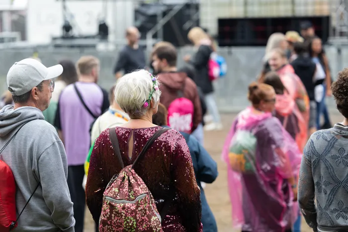 Menschenmenge vor einer Festivalbühne, gesehen von hinten, mit einer Person im Vordergrund mit weißem Haar und einem Paillettenoberteil.