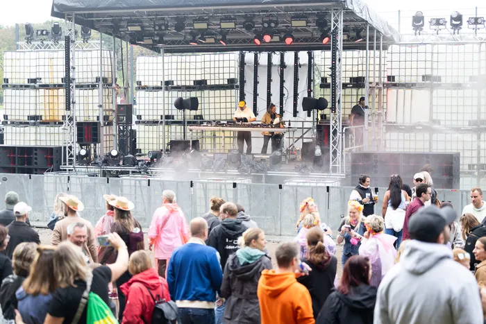 DJ Ante Perry steht an den Turntables auf einer Bühne aus weißen IBC-Containern vor einer Menschenmenge.