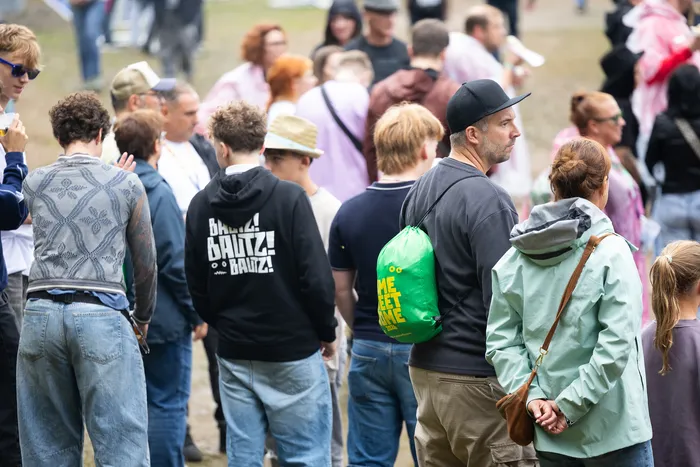 Eine Menschenmenge bei einem Festival, eine Person im Vordergrund trägt einen schwarzen Hoodie mit dem weißen Schriftzug „BAUTZ!“.