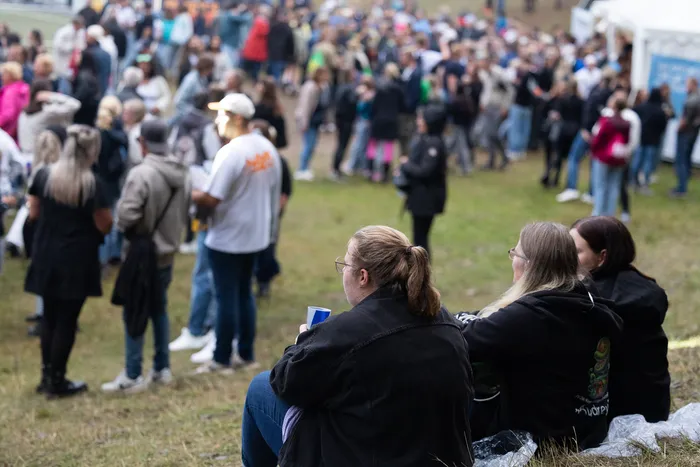 Drei Frauen sitzen mit dem Rücken zur Kamera auf einer Wiese und blicken auf eine große Menschenmenge bei der Bautz 2026.