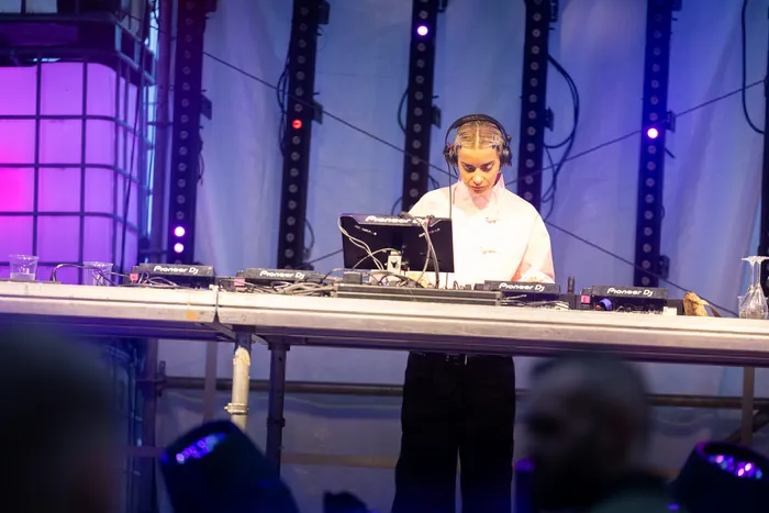 DJ Lovra mit Kopfhörern und weißem Hemd bedient Mischpulte auf der blau beleuchteten Turntable Stage beim Bautz 2026.