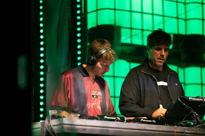 Die DJs Autobahn x Interplay arbeiten an einem Mischpult vor einer grün beleuchteten Wand.