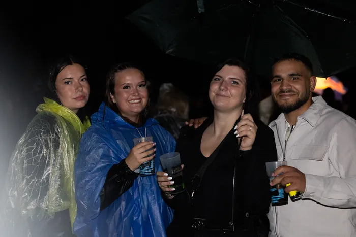Vier lächelnde Personen halten nachts Getränkebecher unter einem Regenschirm bei der Bautz 2026.