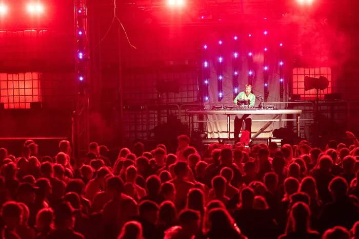 DJ Paracek performt an einem Turntable-Pult vor einer großen Menschenmenge unter intensivem rotem Bühnenlicht.