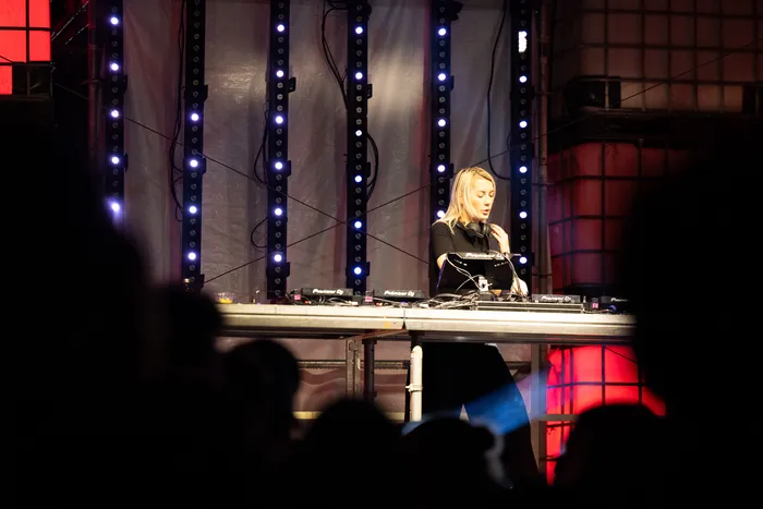 DJ Nusha steht an einem Mischpult vor vertikalen blauen Lichtstreifen auf der Turntable Stage beim Bautz 2026.