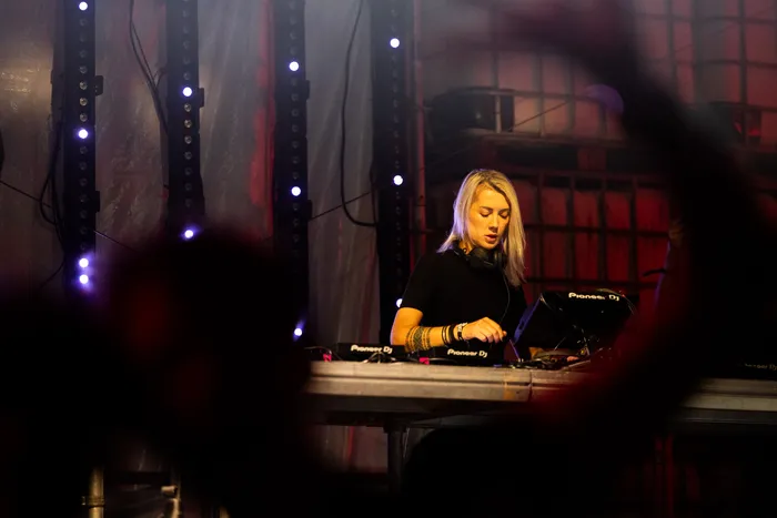 Die DJ Nusha bedient an einem Mischpult vor einer Kulisse mit vertikalen Lichtleisten.