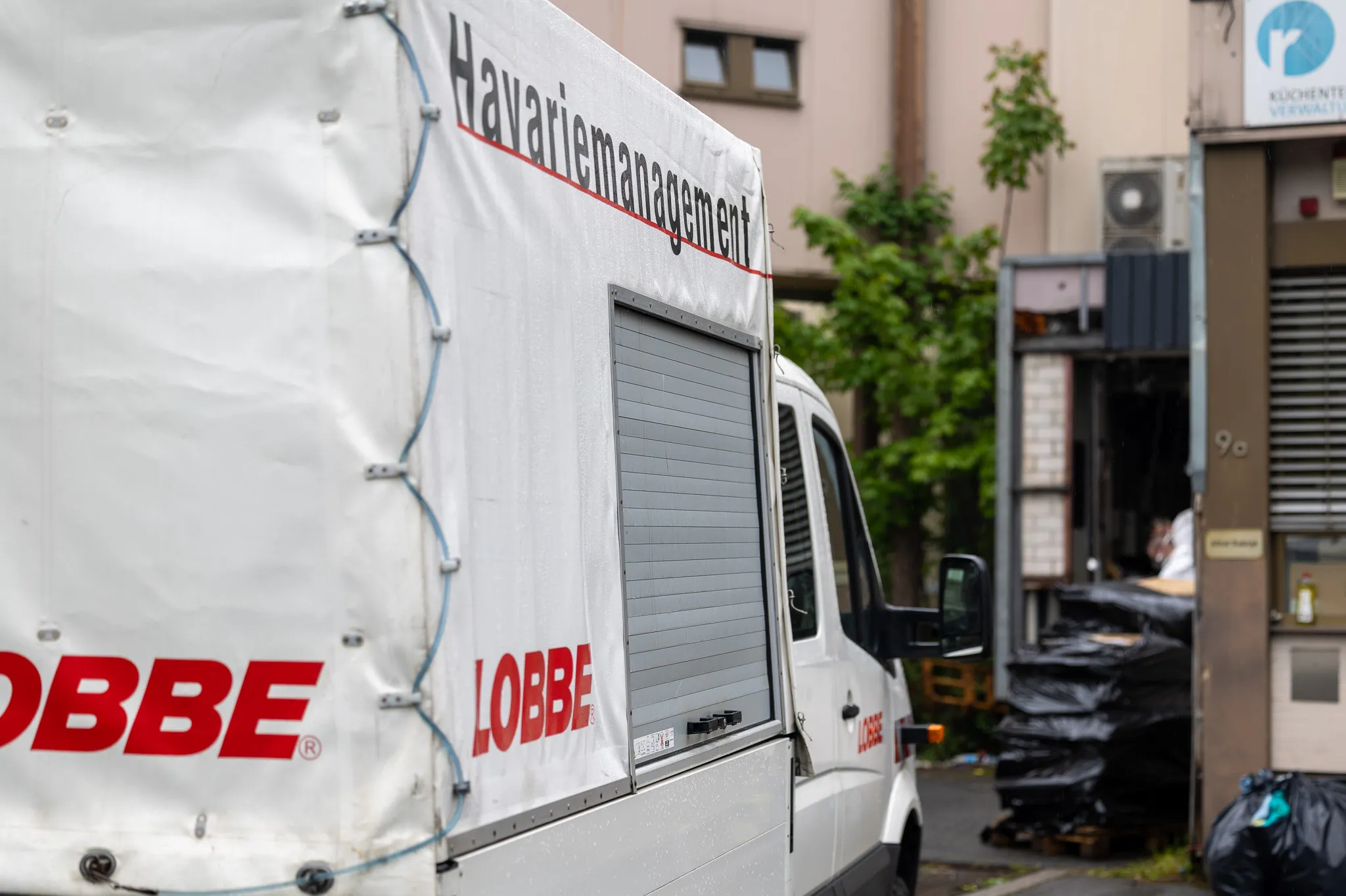 Weißer Transporter des Entsorgungsdienstleisters Lobbe mit Aufschrift „Havariemanagement“ steht vor einem Gebäude, Müllsäcke davor.