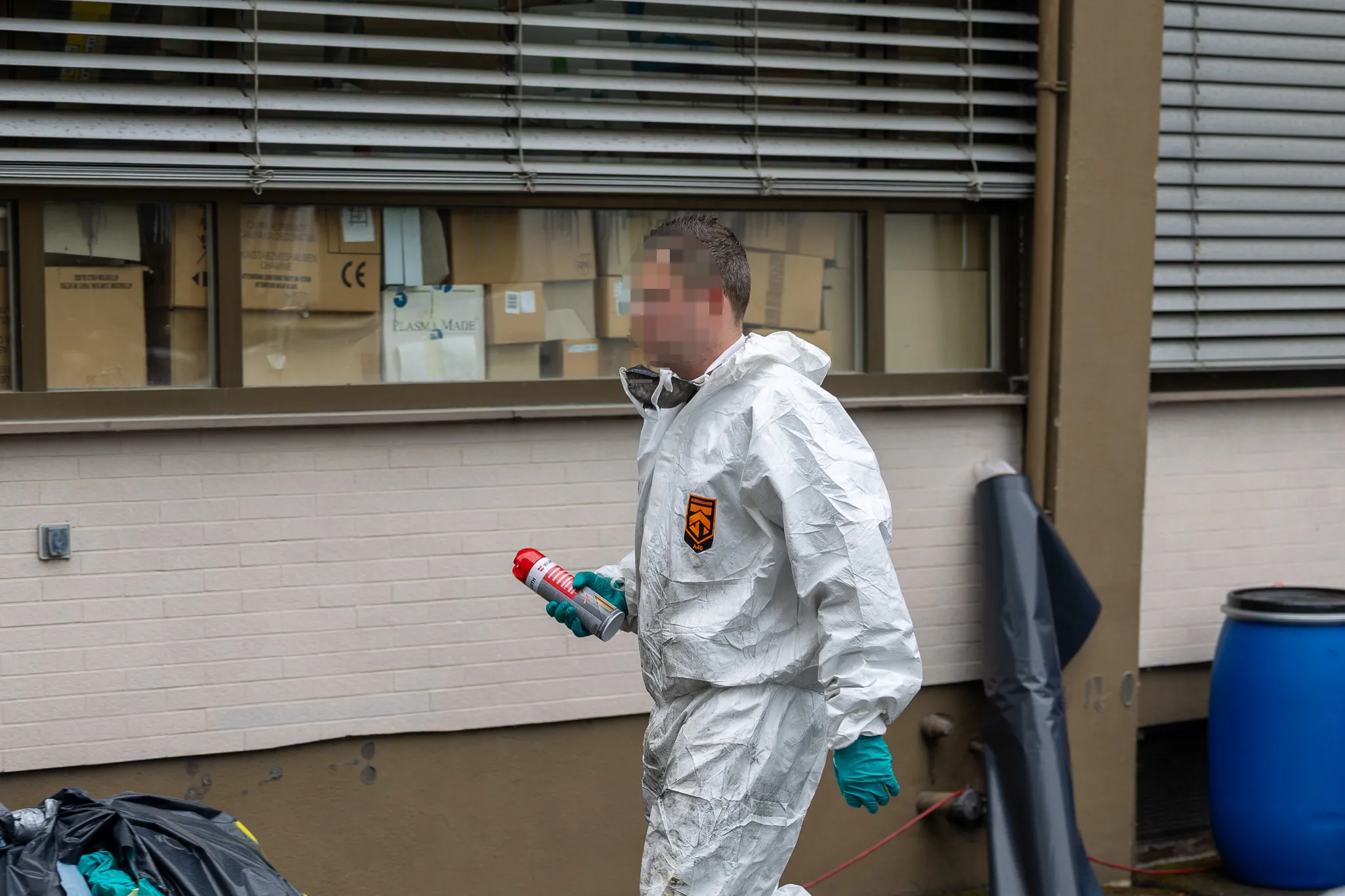 Person in Schutzanzug mit Spraydose vor einem Gebäude, vermutlich bei der Räumung eines Drogenlabors.