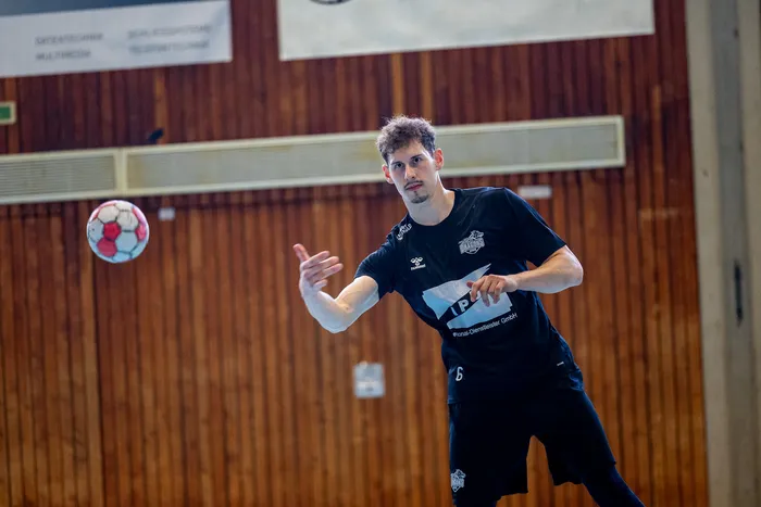 Ein Handballspieler in schwarzem Trikot wirft einen rot-weißen Handball in einer Sporthalle.