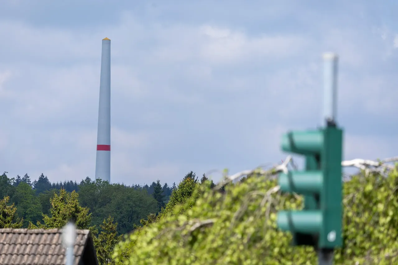 Ein hoher, weißer Turm einer Windkraftanlage mit einem roten Streifen vor einem bewölkten Himmel.