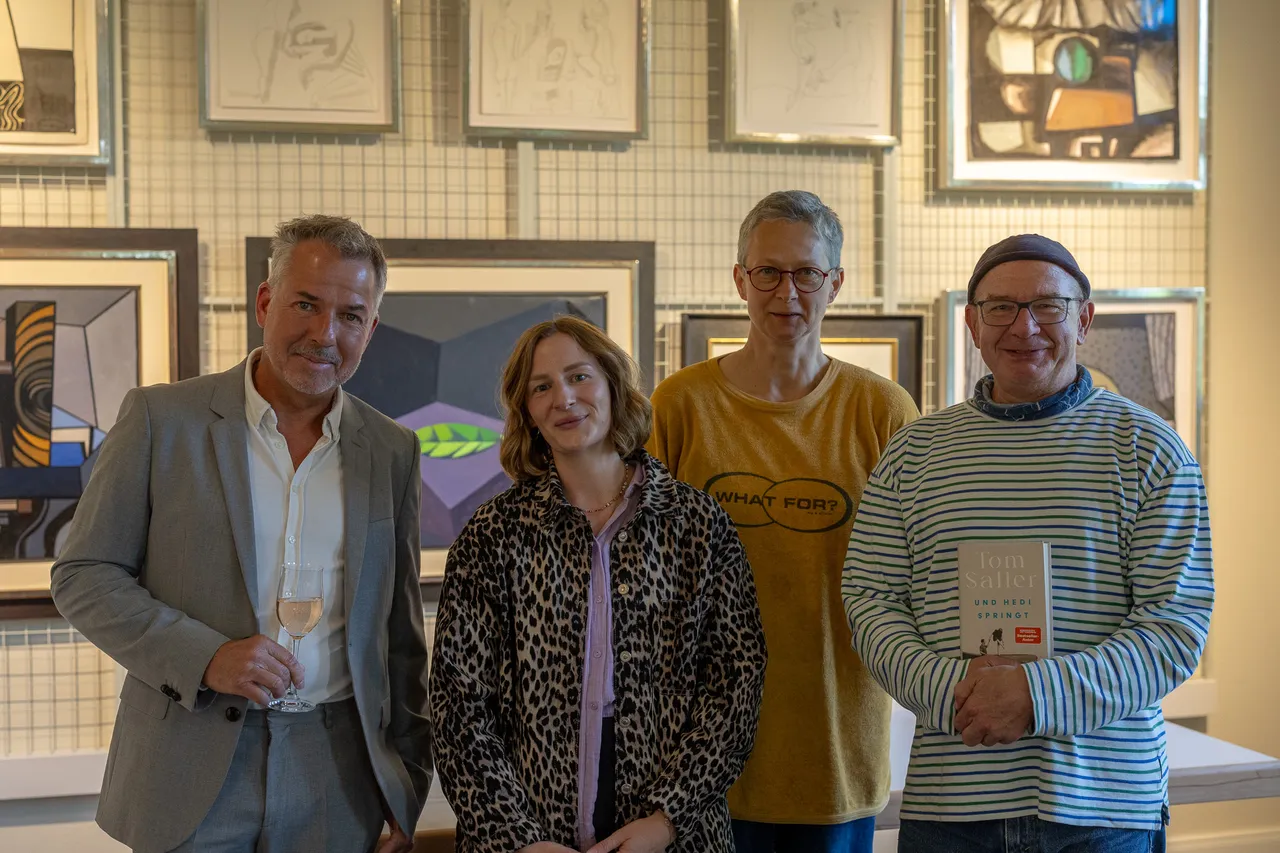 Vier Personen stehen vor einer Wand mit Kunstwerken. Von links: Tom Saller mit Glas, Miriam Buhl-Nordmeier, Jana Eilhardt und Rüdiger vom Brocke mit Buch in der Hand.