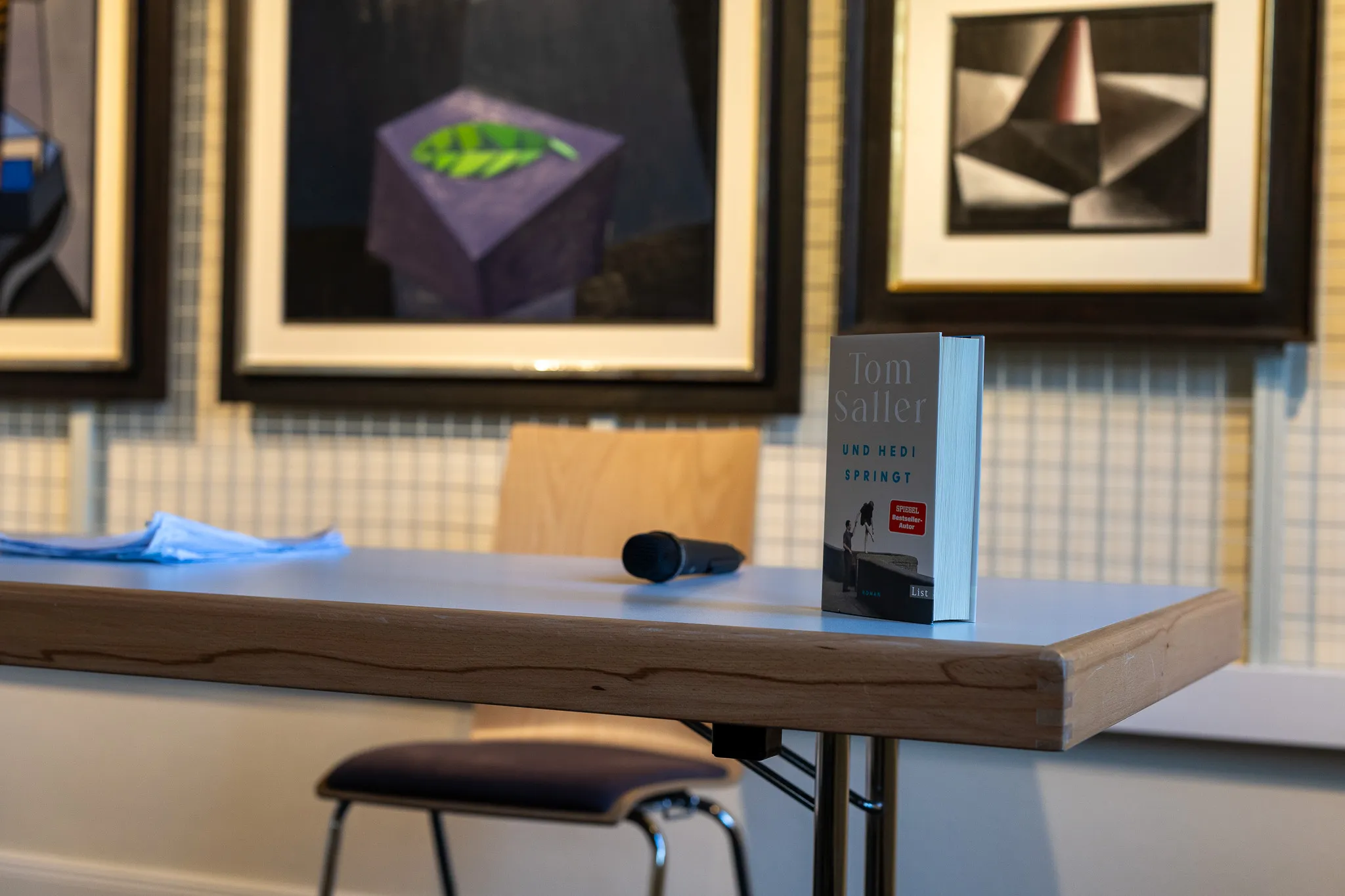 Buch von Tom Saller und Hedi Springt liegt auf einem Tisch vor gerahmten Kunstwerken.