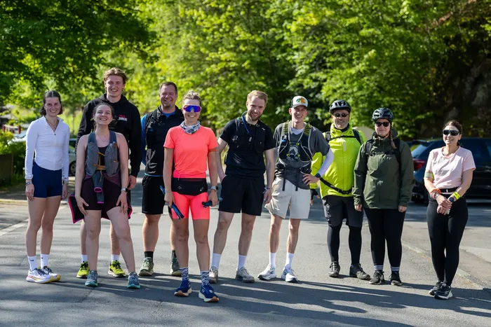 Gruppe von Läufern und Begleitern posiert auf einer Straße, einige tragen Laufkleidung und Rucksäcke.