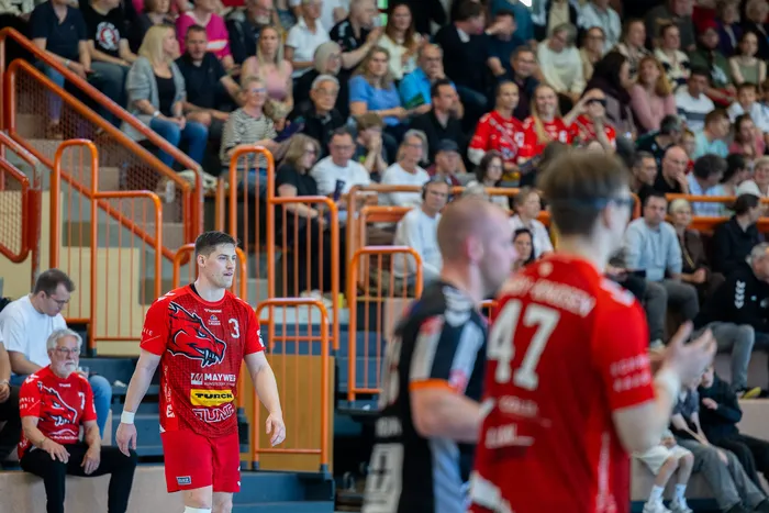 Handballspieler der SGSH Dragons wird nach dem Sieg von Zuschauern gefeiert, im Hintergrund jubelnde Fans in rot und schwarz.