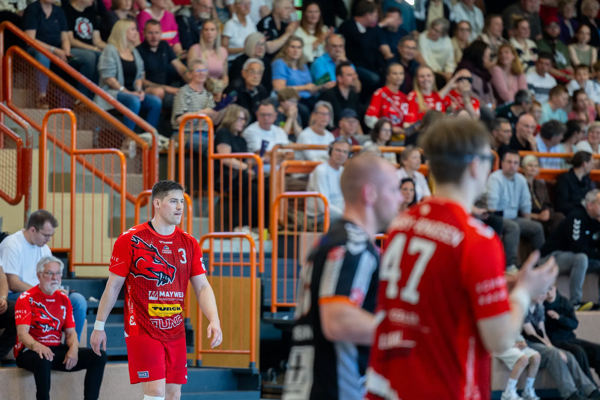 Handballspieler der SGSH Dragons wird nach dem Sieg von Zuschauern gefeiert, im Hintergrund jubelnde Fans in rot und schwarz.