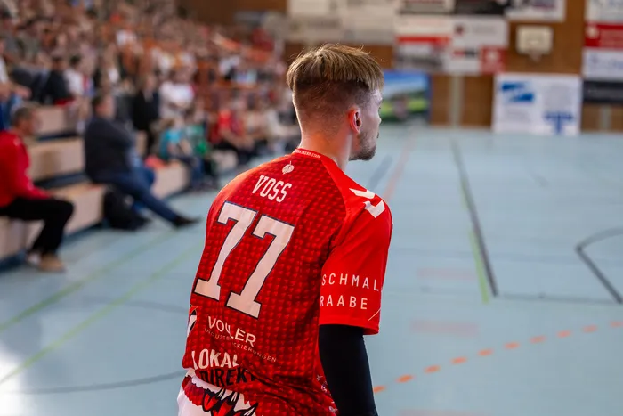 Handballspieler mit der Trikotnummer 77 geht auf dem Spielfeld, im Hintergrund weitere Spieler und Zuschauerränge.