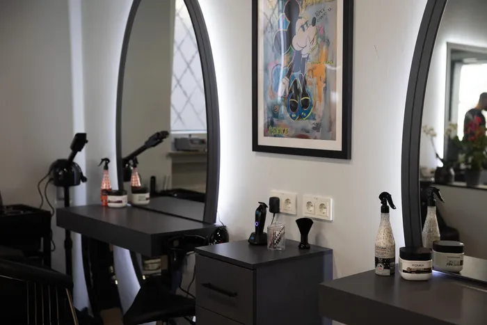 Innenansicht eines Friseursalons mit großen ovalen Spiegeln, Stylingprodukten auf dunklen Ablagen und einem gerahmten Bild an der Wand.