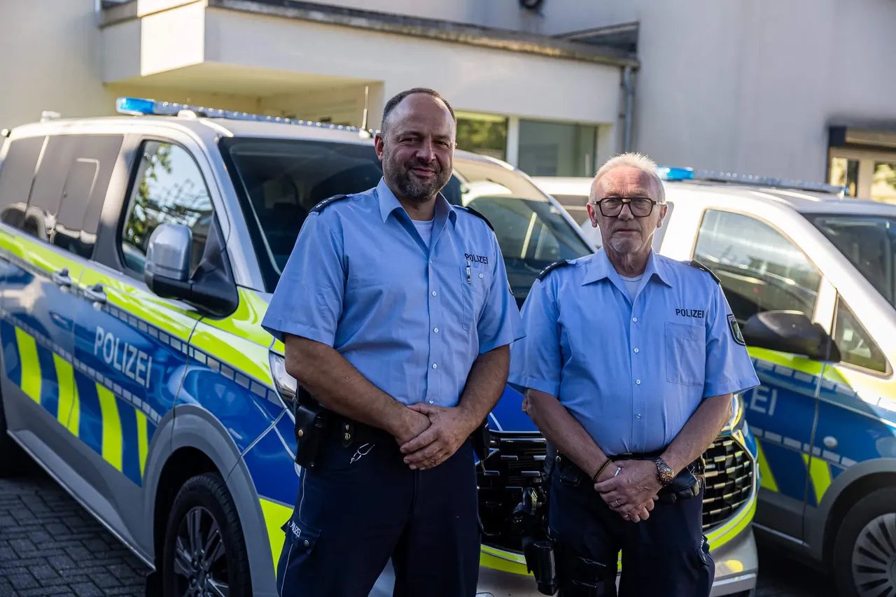 Zwei Polizisten in blauen Uniformen stehen vor einem blau-gelben Polizeifahrzeug.