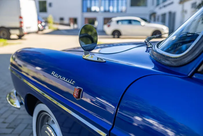 Nahaufnahme der blauen Motorhaube eines Renault Oldtimers mit Markenschriftzug und einem runden Außenspiegel.