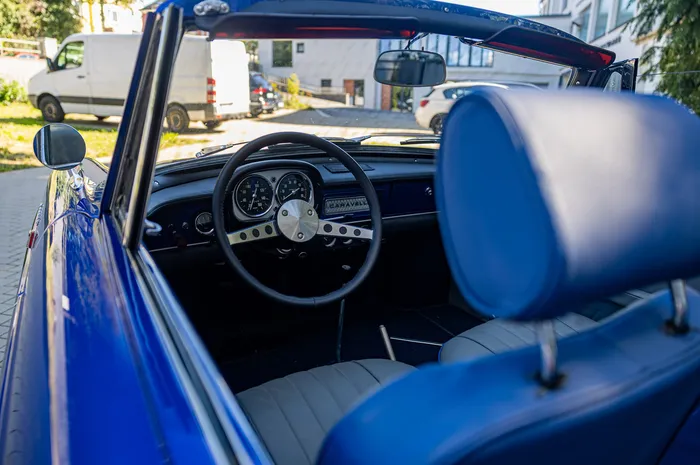 Innenansicht eines blauen Oldtimer-Cabriolets mit schwarzem Lenkrad, Armaturenbrett und blauen Sitzen.