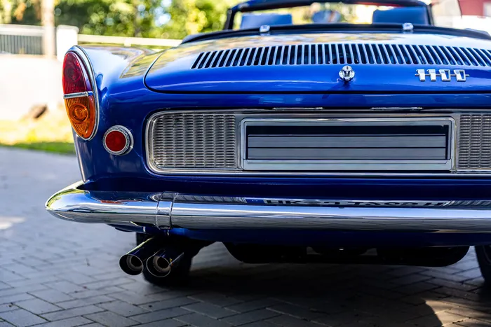 Rückansicht eines blauen Oldtimers mit Chromstoßstange, Doppelendrohr und der Modellbezeichnung „1100“.