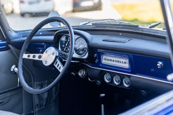 Innenraum eines blauen Oldtimers mit schwarzem Lenkrad, analogen Instrumenten und dem Schriftzug „CARAVELLE“ auf dem Armaturenbrett.
