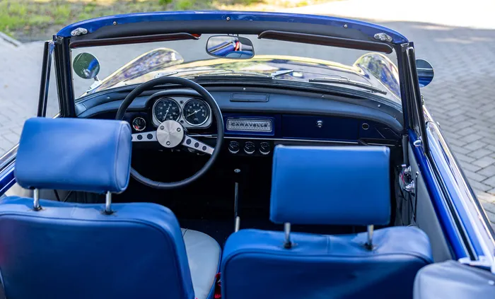 Innenraum eines blauen Oldtimer-Cabriolets mit blauen Ledersitzen und einem Armaturenbrett mit analogen Anzeigen.
