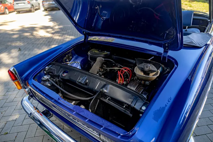 Blick in den Motorraum eines blau lackierten Oldtimers mit geöffneter Motorhaube und sichtbaren Motorkomponenten.