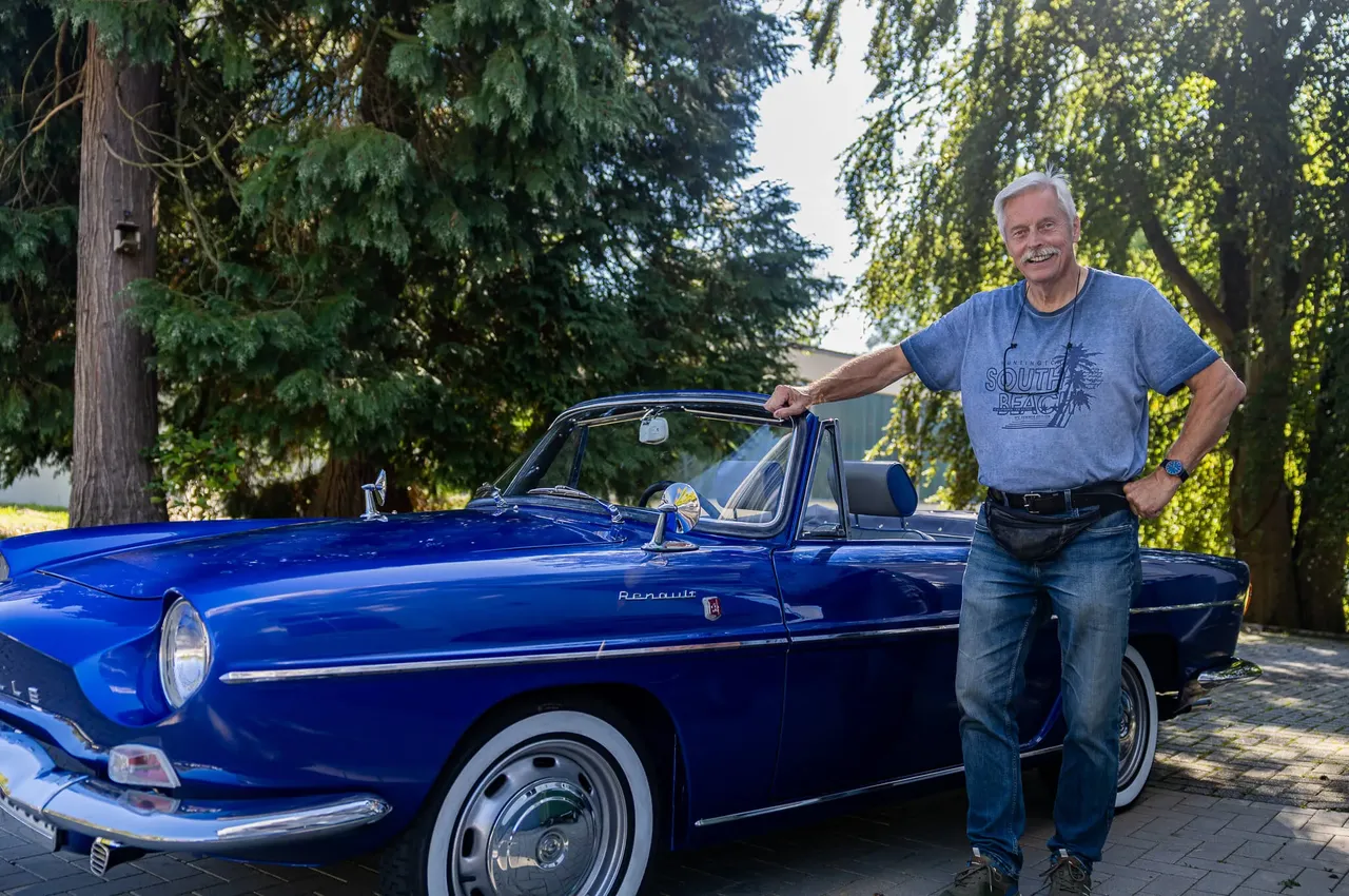 Wilfried Gerdel steht lächelnd neben einem blauen Renault Cabriolet vor einer Kulisse aus Bäumen.