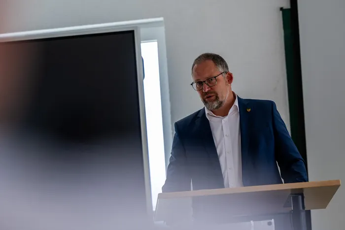 Bürgermeister Armin Kibbert spricht vor einem Publikum, steht an einem Rednerpult und trägt einen dunklen Anzug mit einer Anstecknadel.