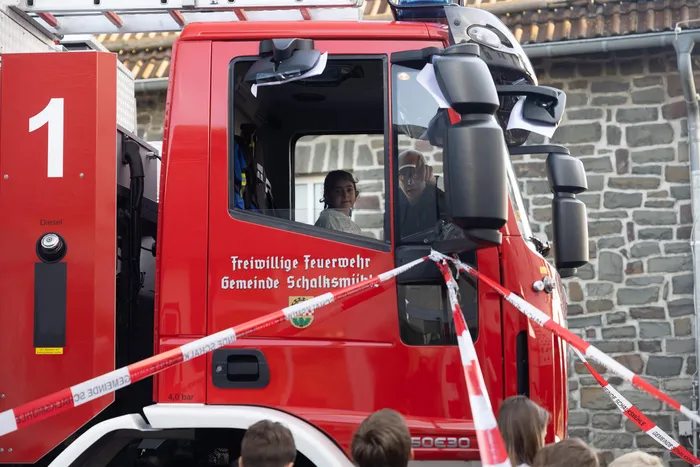 Ein Kind blickt aus dem Fenster eines roten Feuerwehrautos der Freiwilligen Feuerwehr Schalksmühle hinter rot-weißem Absperrband.